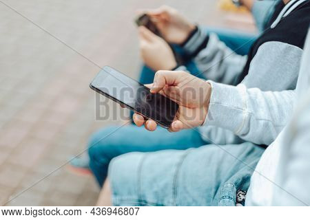 Attractive People Family Of Different Ages Use A Smartphone While While Sitting Together On A Bench 