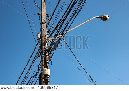Public Lighting Electric Network Pole With A Tangle Of Wires, With The Lamp Rod And The Blue Sky In 