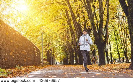 Fit Athletic Woman Have A Running In The Autumnal City Park. Young Fitness Female Smiling And Runnin
