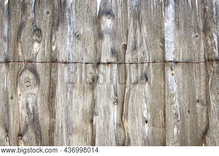 Texture Of An Old Fence Made Of Dried And Cracked Wooden Panels With Rusty Barbed Wire On Top Of It 