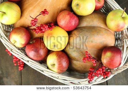 Juicy apples and pumpkin in wooden basket on table close-up