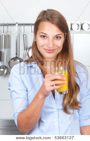 Smiling woman in the kitchen drinking orange juice