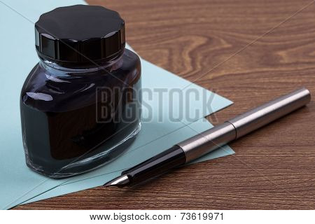 Inkwell and fountain pen on wooden texture.