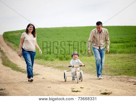 Family with little boy on tricycle in nature