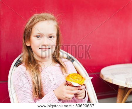 Cute little girl eating a muffin in a cafe