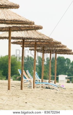 Row Of Straw Umbrellas And Suneds At A Beach. Photo With Untraditional Color Rendering For Artisctic