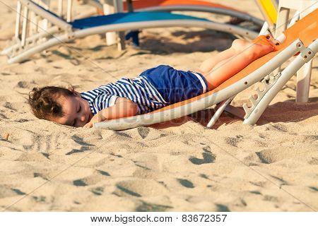 Sweet Toddler Dressed As A Sailor Lying From A Top Of A Sunbed On A Beach And Looking As He Is Drunk