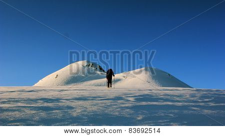 man goes on a snowy slope in the mountains with ice axe