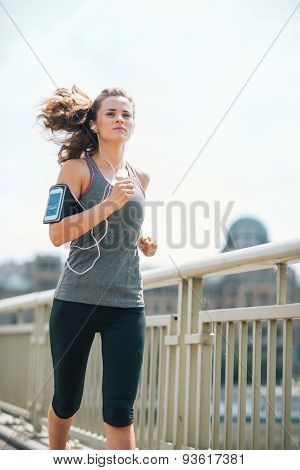 Long-haired Woman Jogging On Bridge Listening To Music In Summer