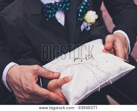 Father hands help young boy to carry a pillow with wedding rings during wedding ceremony