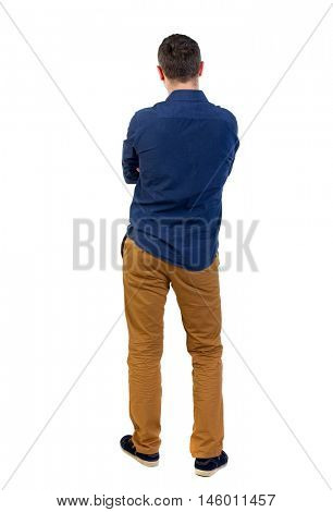 Back view of man . Standing young guy. man in a blue shirt with the sleeves rolled up, standing with her hands folded on his chest.