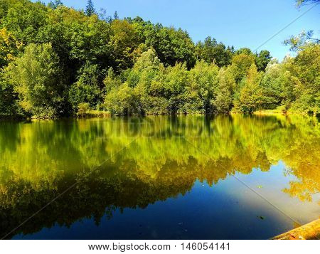 Lake with reflection and deciduous forest in wild nature during beautiful sunny day