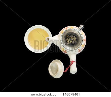 Closeup beautiful ceramic tea pot with dried tea leaves on tea strainer and brown tea in a cup of tea isolated on black background in top view with clipping path
