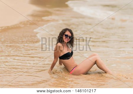 Sexy tanned  fit girl in black bikinii on blue ocean background. Young curly hair woman on the tropical beach.  Woman in bikini at tropical beach.
