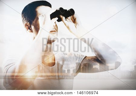 Young male looking binoculars on abstract city background with sunlight. Double exposure