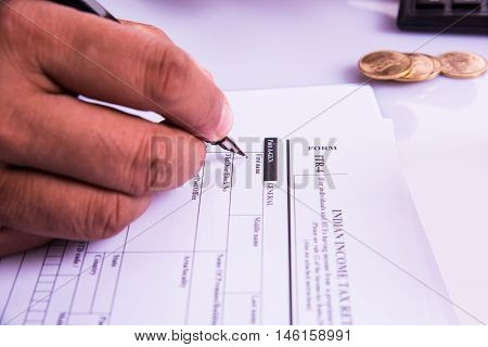 Indian man or accountant person filing Indian income tax returns form or ITR document showing indian currency, house model, toy car and calculator over white table top, selective focus