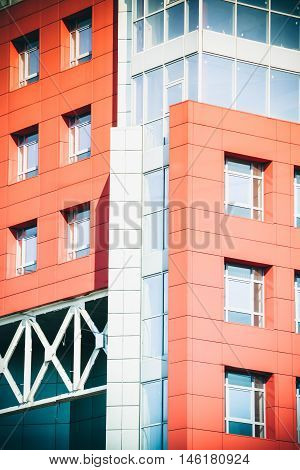 Part of the facade of a modern building with red walls square windows the blue mirrored glass. Architecture in a modern style and high-tech on a bright sunny day