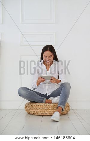 Young attractive businesswoman sitting with crossed leg and holding tablet on a hassock, she is wearing casual outfit