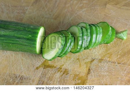 Cucumber and slices on a wooden cutting board.