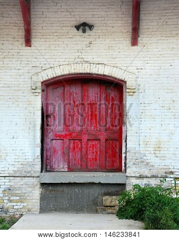 Rustic red wooden door is framed by white painted bricks. Doorway is part of old train station in Stoughton Wisconsin.