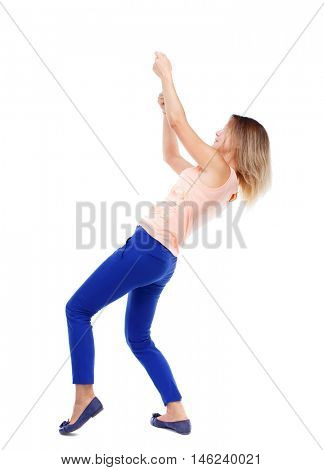 back view of standing girl pulling a rope from the top or cling to something. Isolated over white background. The blonde in a pink shirt pulling the rope from above.
