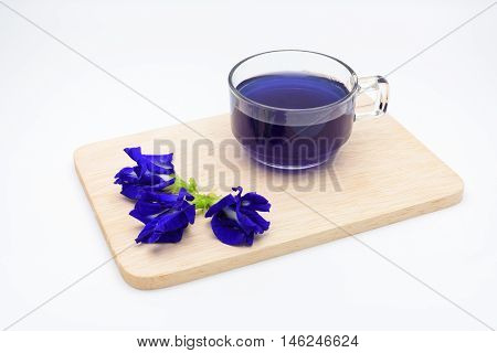 Butterfly pea juice with pile of pea flower on wooden plate on white background.