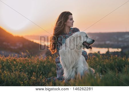Young woman sitting with her dog enjoying sunset.