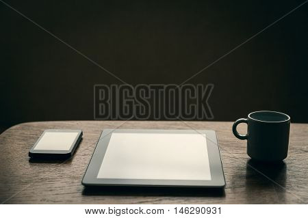 Blank tablet blank smartphone and hot cup of coffee on wooden table. Close-up.