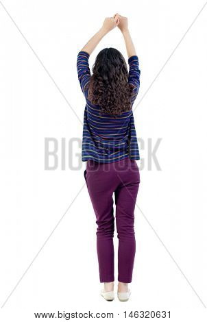 back view of dancing young beautiful woman. Long-haired curly girl in a blue sweater pulls his hands up.