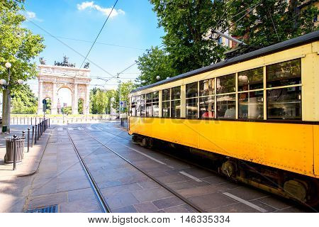 Street view with old yellow tram and Simplon city gate in Milan