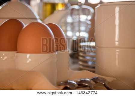 Close up of eggs in holders beside spoons and clean dishware ready for breakfast setting