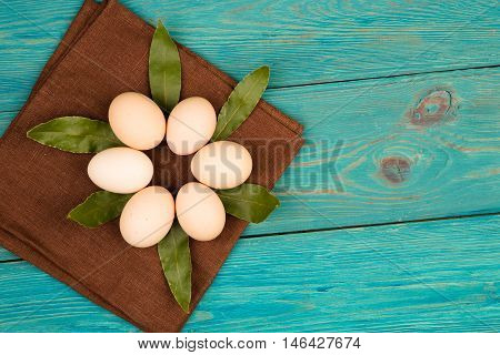 Chicken Eggs, Bay Leaf And Brown Linen Napkin On Blue Wooden Table