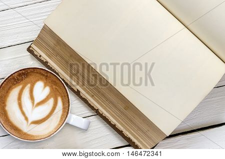 Cup of coffeelatte art and old blank book on wooden background.