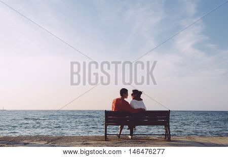 back portrait of young couple looking at each other on bench by the sea in Kusadas, Turkey, clean composition
