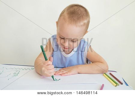 Little boy at a desk learning to draw with markers and pencils. Child with a felt-tip pen in hand. Photo with limited depth of field.