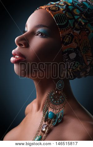young beautiful fashion model with traditional african style with scarf, earrings and makeup on dark blue background.