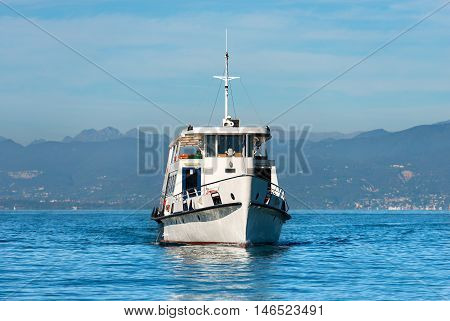 Ferry boat during navigation in front of the town of Lazise in the Garda Lake Veneto Italy. In the background the coast of Lombardy