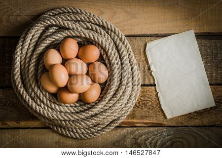 Eggs in a basket made from rope and blank paper on a wooden table