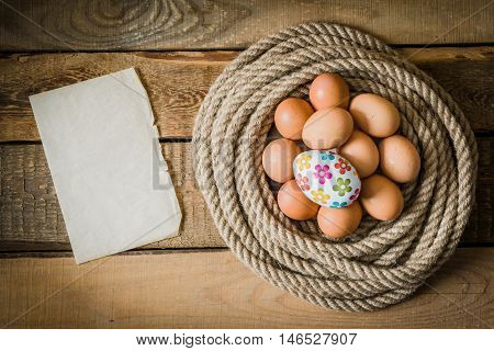 Eggs in a basket made from rope and blank paper on a wooden table