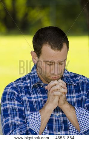 Man praying outdoors with a bright yellow and green sunlight background.