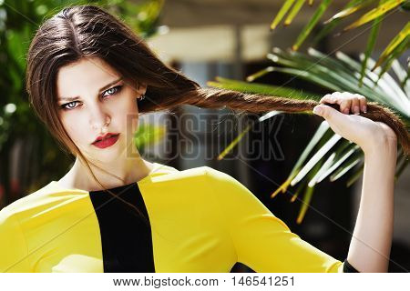 Outdoor portrait of young beautiful fashionable lady posing on the street. Model wearing stylish yellow summer dress. Girl looking at camera. Female fashion concept. City lifestyle. Sunny day. Close up.