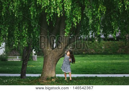 Little cute girl running around near the big tree