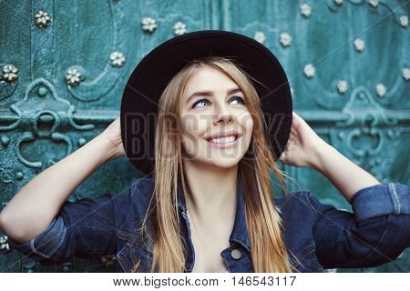 Street fashion portrait of a beautiful young lady smiling and looking up. Model wearing stylish wide-brimmed hat. City lifestyle.