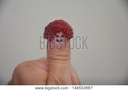 Red raspberry on the thumb with a smiling face on a light background