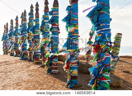 Traditional wooden poles to the hitching post serge. Prayer flags. Buryat tradition on the shores of Lake Baikal in the winter mountains in the background. Winter Landscape on Olkhon island. Buryat Region, Russia, Siberia.