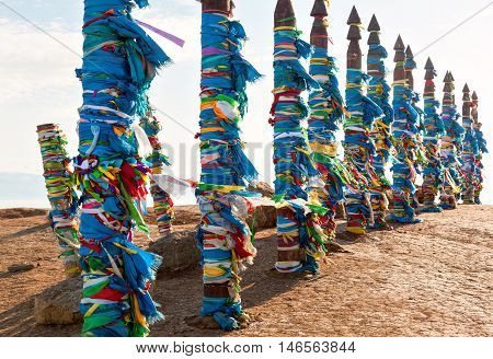 Traditional wooden poles to the hitching post serge. Prayer flags. Buryat tradition on the shores of Lake Baikal in the winter mountains in the background. Winter Landscape on Olkhon island. Buryat Region, Russia, Siberia.