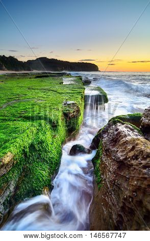 The wave flows over weathered rocks and boulders at Turimetta Beach rock shelf on sunrise. Sydney Australia