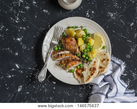 Lemon thyme baked chicken potatoes and green peas on a white plate on a dark background. Delicious lunch