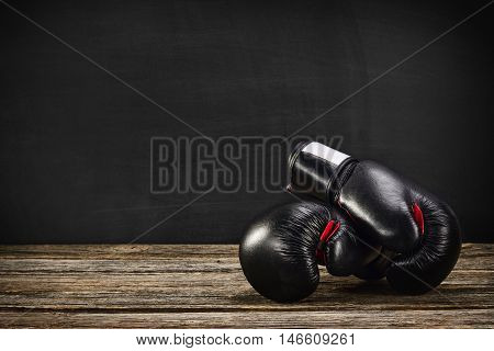 Pair of boxing gloves on a vintage wooden desk with chalkboard background. Concept image, the idea of brutal competition.