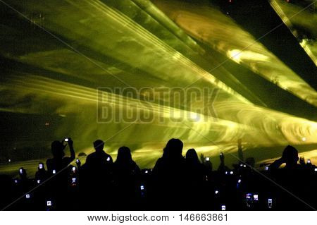 Silhouetted crowd attending laser show. Streaks of light projected overhead.